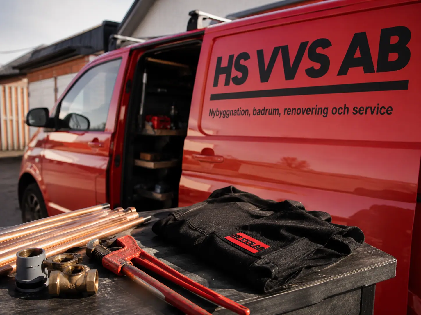 VVS-verktyg, kopparrör och arbetskläder framför HS VVS AB:s servicebil